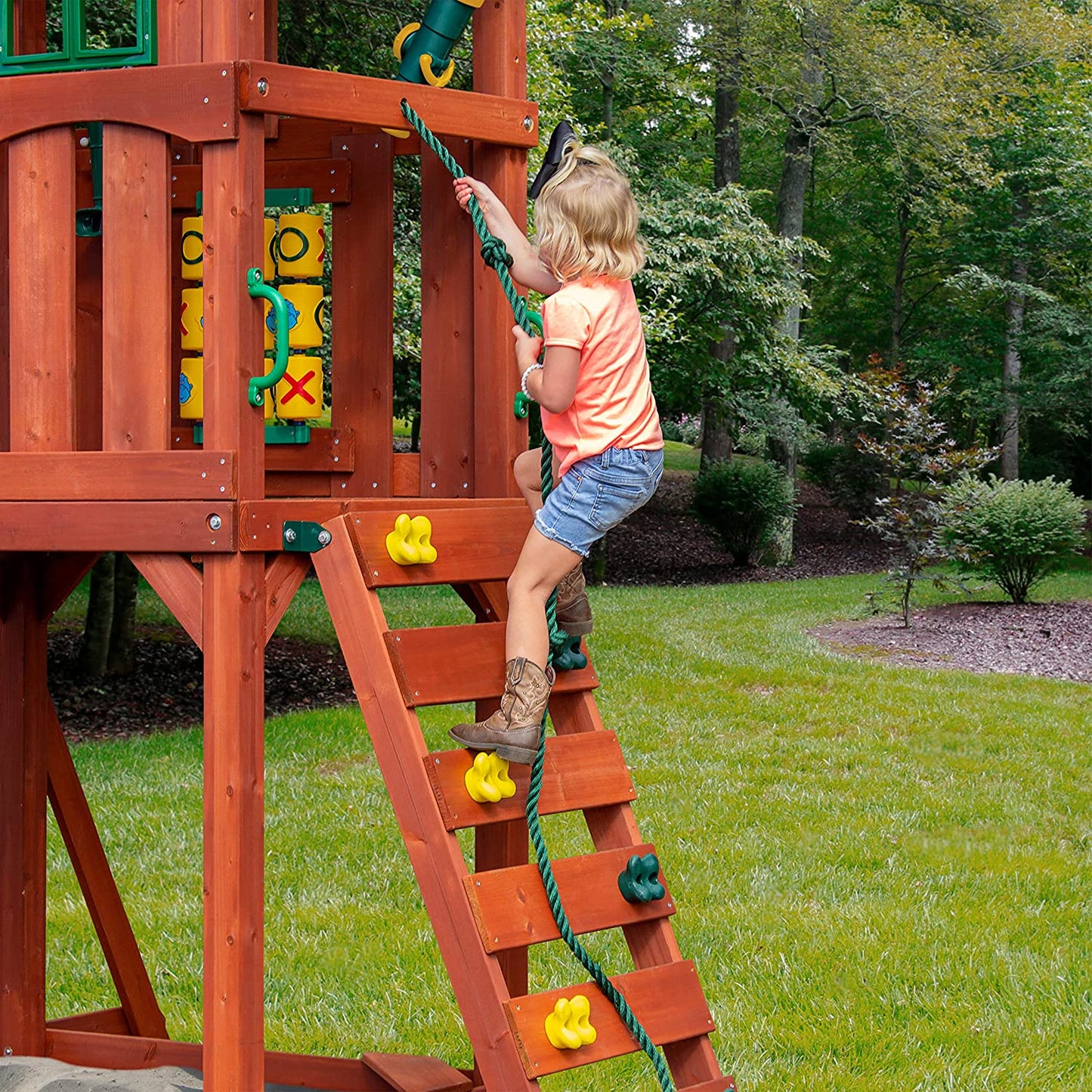 A close up of a child climbing up a small rock wall of a kids wooden outdoor playset.