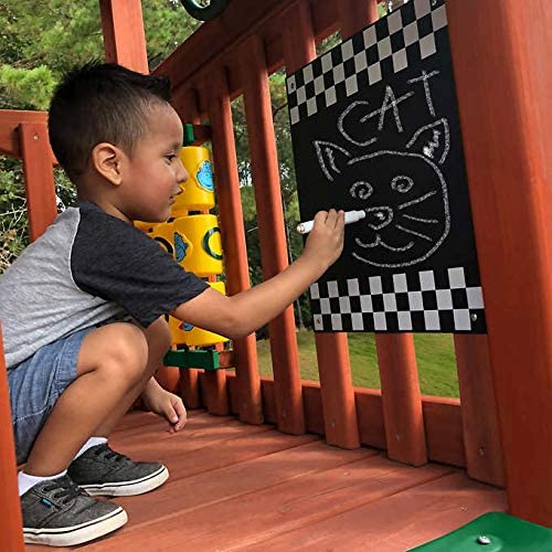 A child is drawing a cat on a chalkboard which is part of a large outdoor wooden play-set for kids.