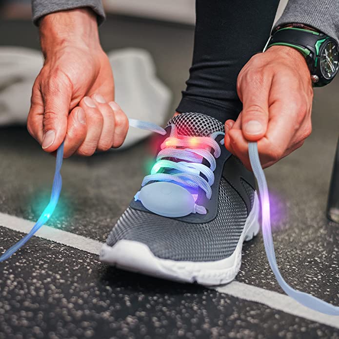 A close-up of a show with LED light-up laces. A pair of hand is about to tie up the laces which are lit up in multi-colors,