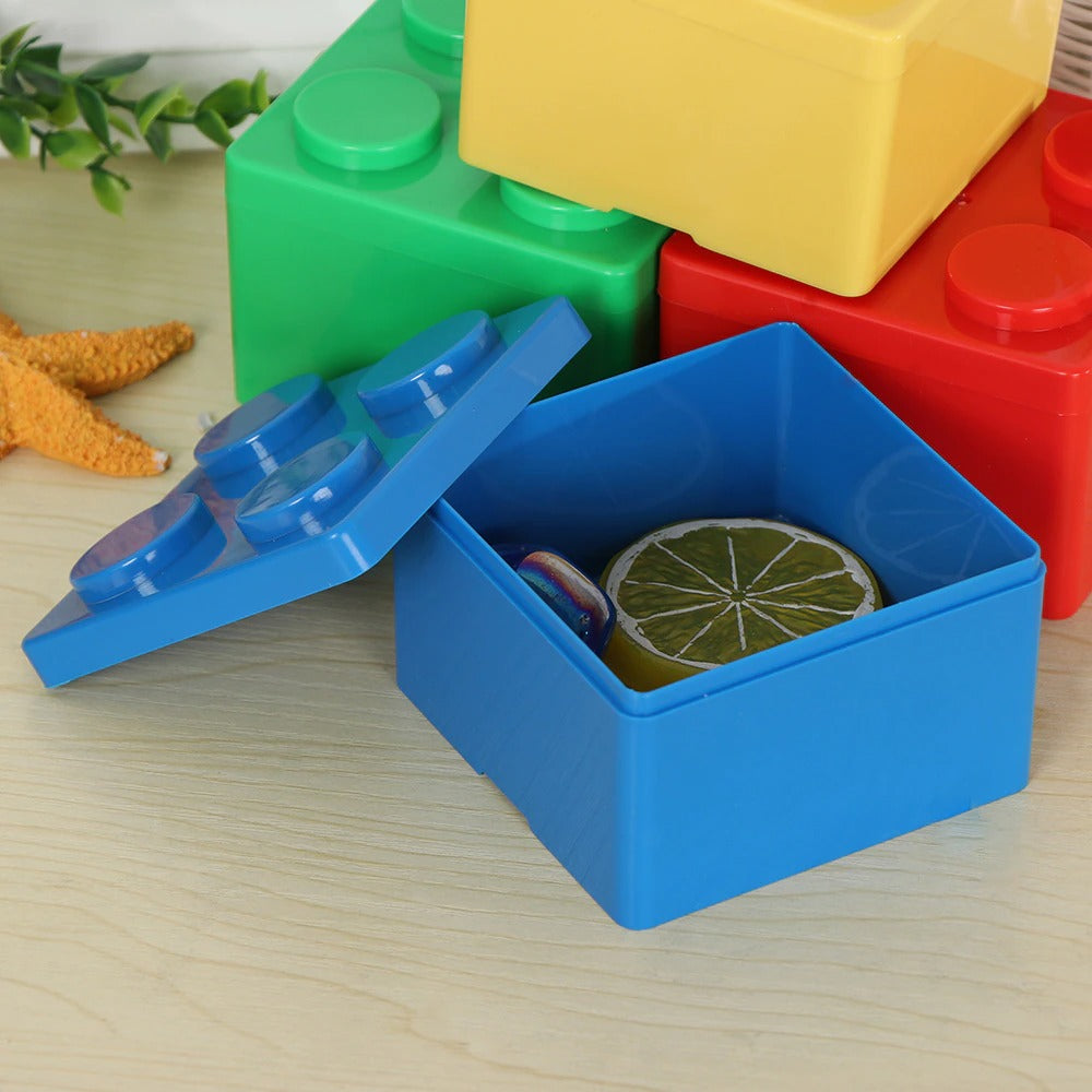 Several storage boxes which look like giant Lego pieces. There is a blue box which is filled with 2 toys and three other Lego storage boxes are in the background. They are red, yellow and green.