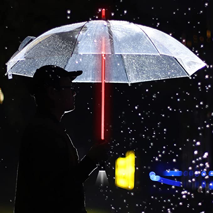 A person is holding a clear colored umbrella in the dark which has a red handle that is lit up like a lightsaber.
