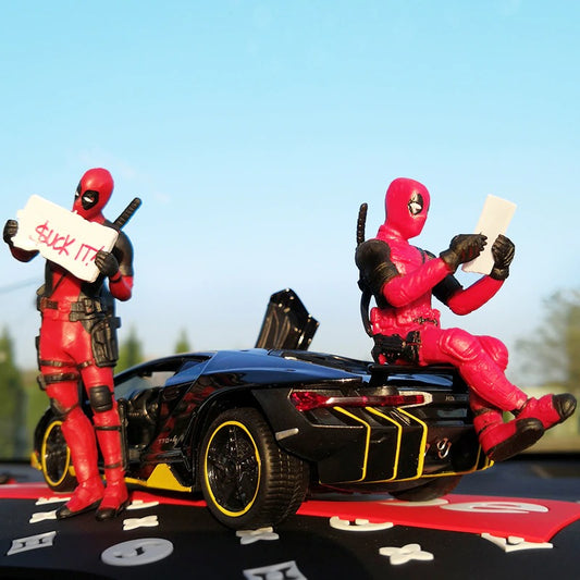 Two Marvel Deadpool action figures posed with a black car with yellow stripes. One figure is reading and another is holding a sign saying, ‘Suck It’