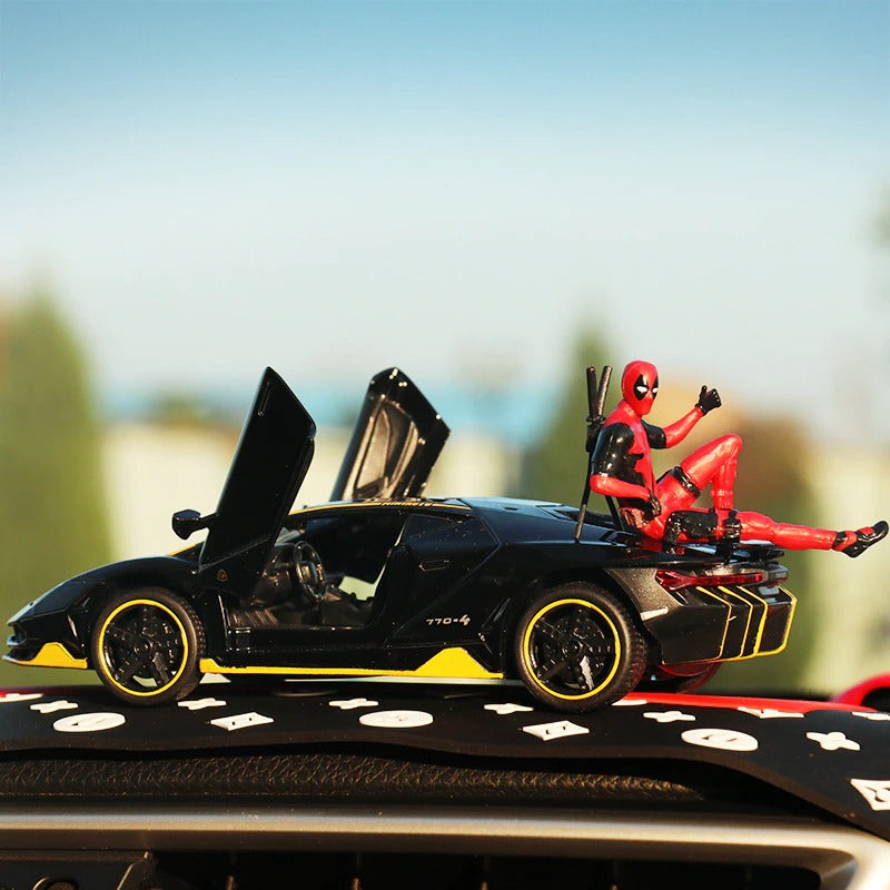 A Deadpool action figure sitting on the back hood of a black toy car. He has been posed with his thumb up in the air.