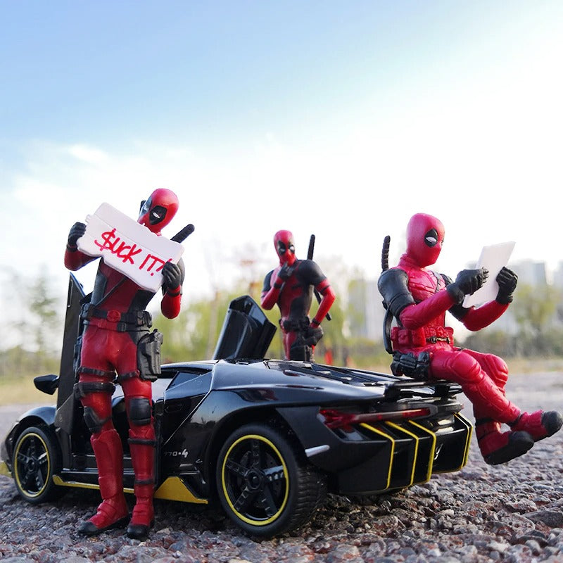 Three Deadpool action figures posed with a black miniature car. One figure is sitting on the back of the car reading. Another is holding up a sign saying, ‘Suck It’ and the other is posed as if he is looking behind him and thinking about something.