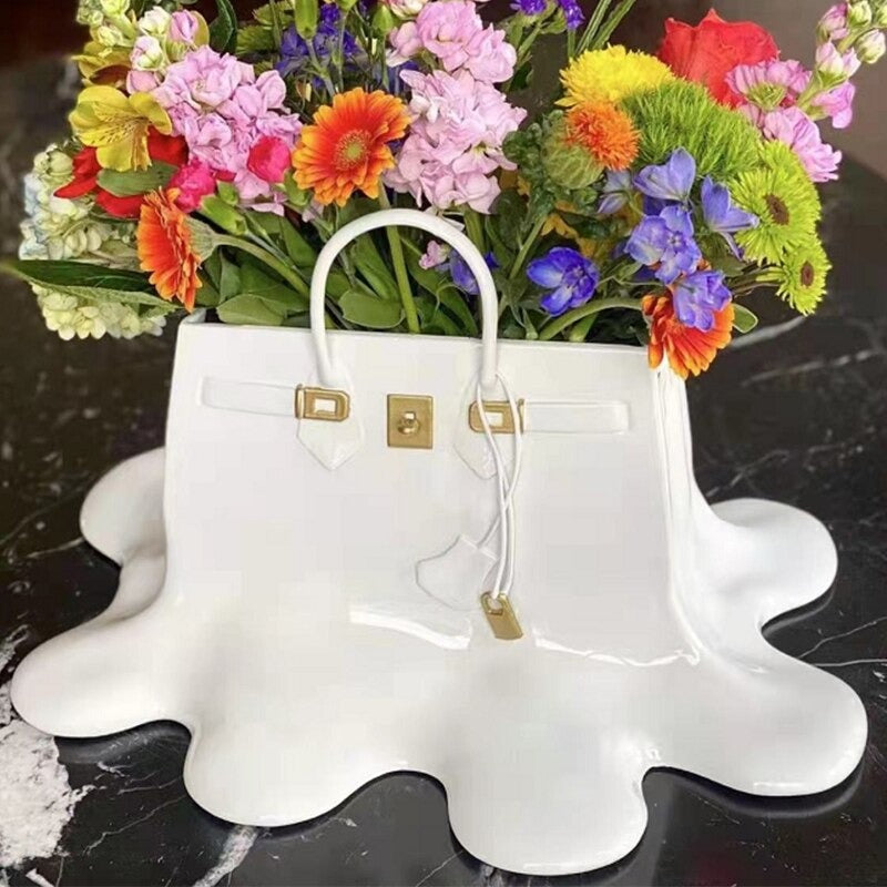 A white colored resin vase which looks like a melting designer women’s handbag. The vase is filled with a colorful bouquet of different flowers.