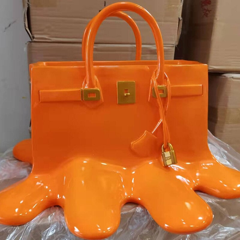 An orange colored vase which looks like a melting women's designer handbag. The handbag has gold embellishments.