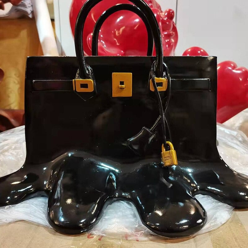 A black vase which looks like a woman’s handbag is melting. The handbag has gold painted embellishments.