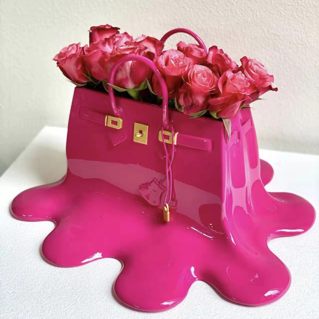 A pink resin vase which looks like a melting designer women’s handbag. The vase is filled with a pretty bunch of pink roses