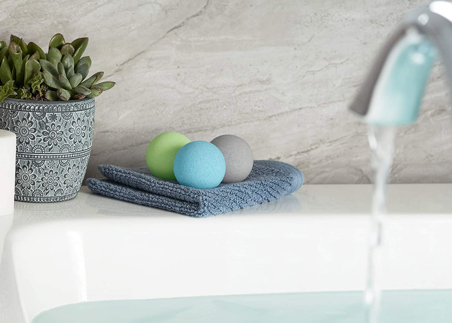 Three different colored bath bombs for men resting on a towel on the edge of a bathtub.