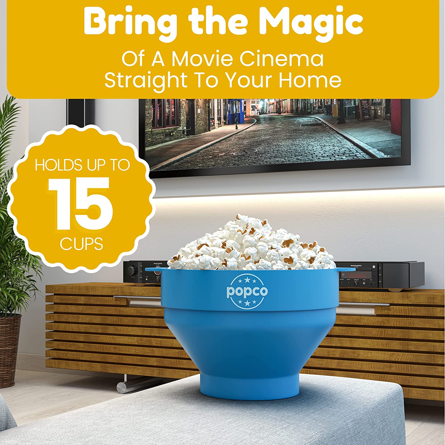 A microwave popcorn maker filled with fresh popcorn. The popcorn maker is sitting on an ottoman in front of a TV. There is text which says, 'Bring the magic of a movie cinema straight to your home.'