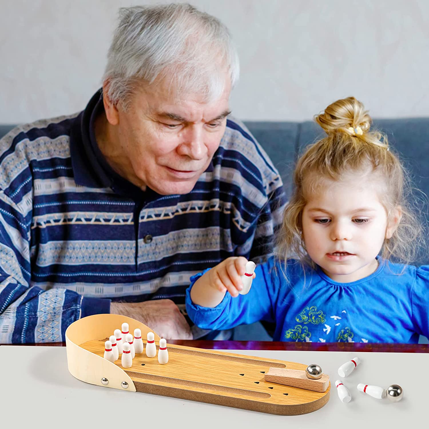 A man and a child are playing with a mini tabletop bowling game.