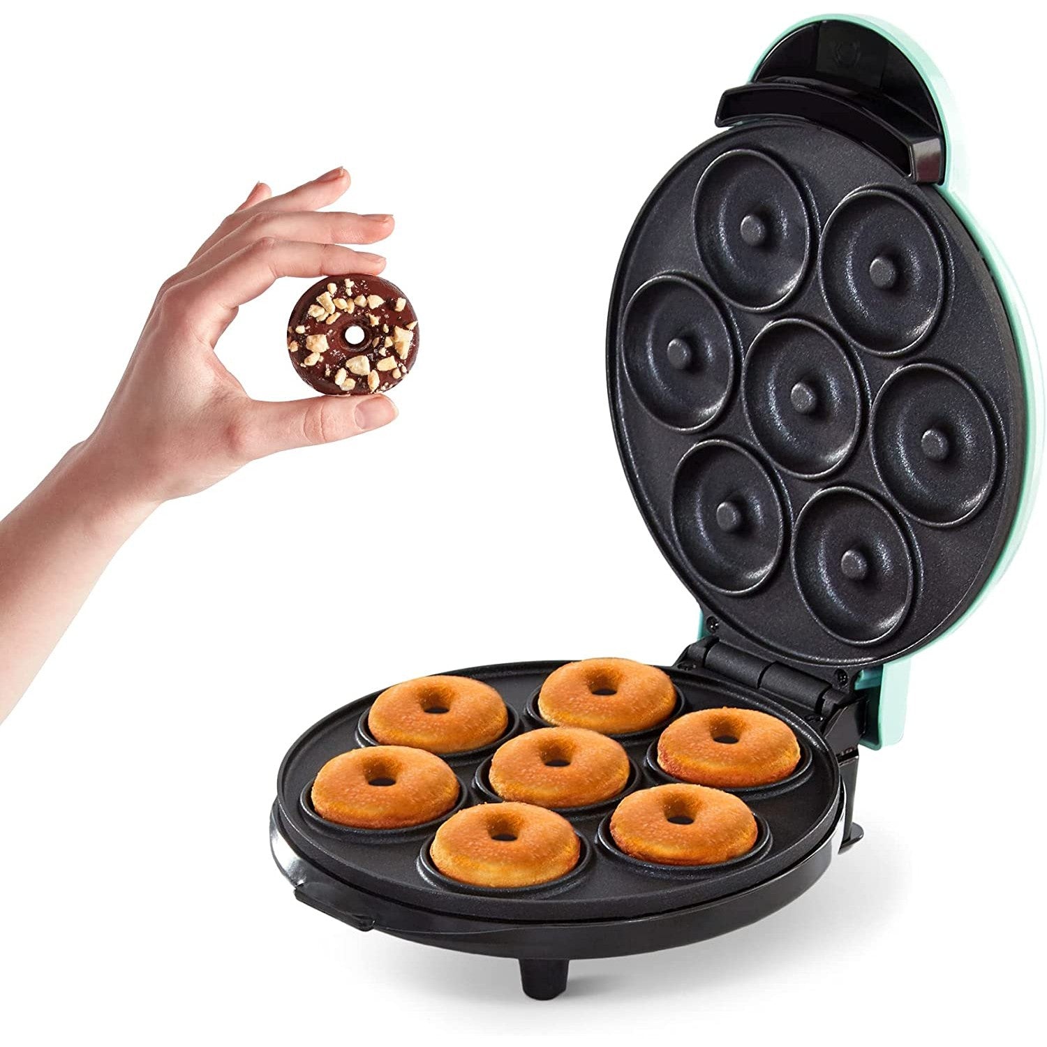 A mini donut maker with 7 freshly baked donuts inside the machine. A hand is holding a chocolate covered donut.