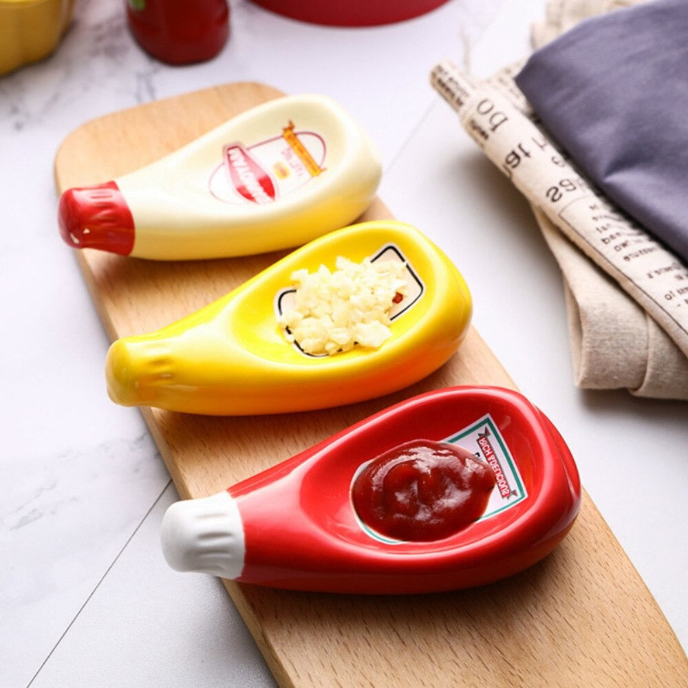 Three dipping bowls which look like miniature versions of larger sauce bottles which include mayo, ketchup and mustard. The ketchup bowl has tomato sauce in it, the mustard bottle has garlic in it and the mayo bottle is empty.