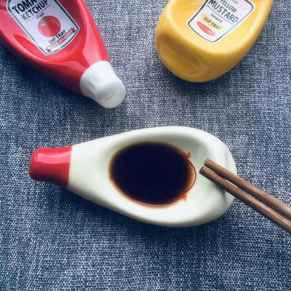 Three sauce dipping bowls which look like tiny versions of mayonnaise, tomato sauce and mustard which are used for dipping sauces for food. The mayo dipping bowl has soy sauce in it.