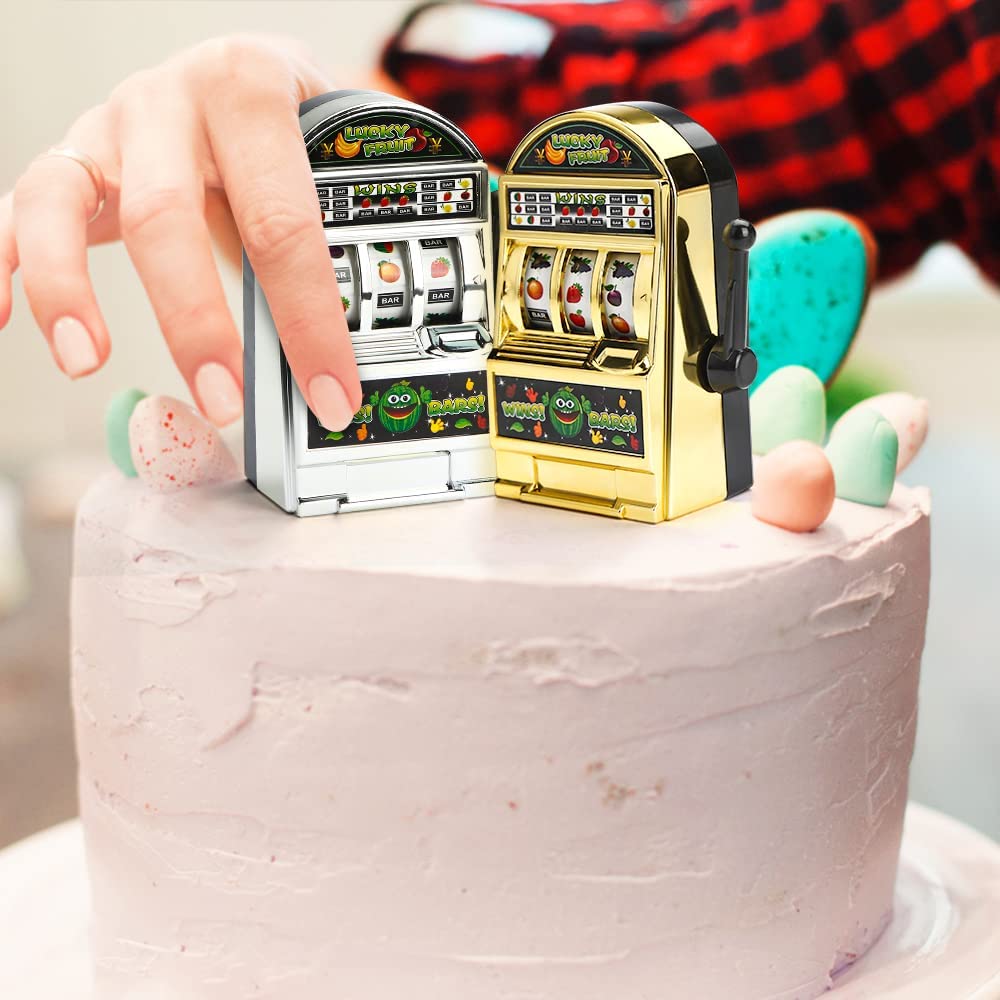 A silver and gold mini slot machine toy being placed on top of a birthday cake.