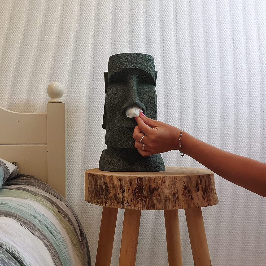 A moai shaped tissue box holder with a hand pulling a tissue out of its nsoe.