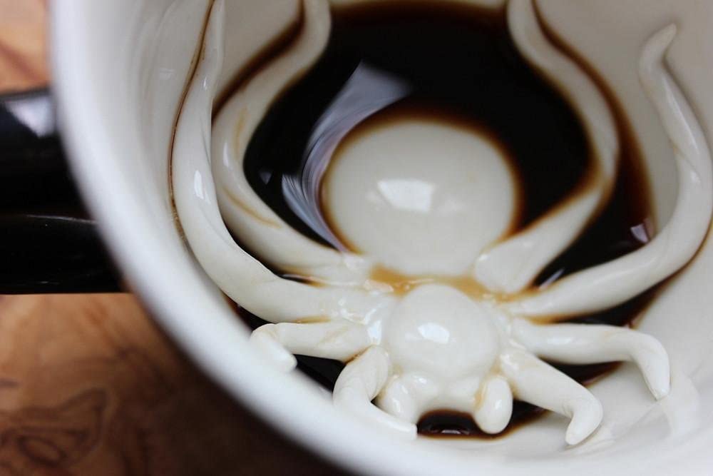 A close up view of a coffee cup with a fake ceramic spider hidden at the base of it.