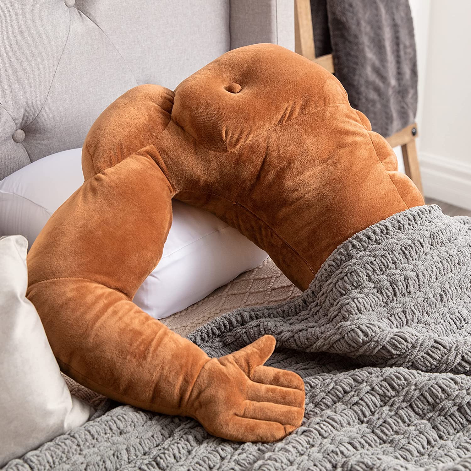 A muscle man pillow is half-tucked under a blanket on a bed.