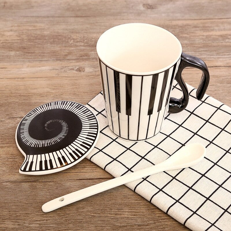 A music inspired mug and lid. The mug and lids have a piano keyboard printed on them. There is a long white spoon next to the mug and lid.