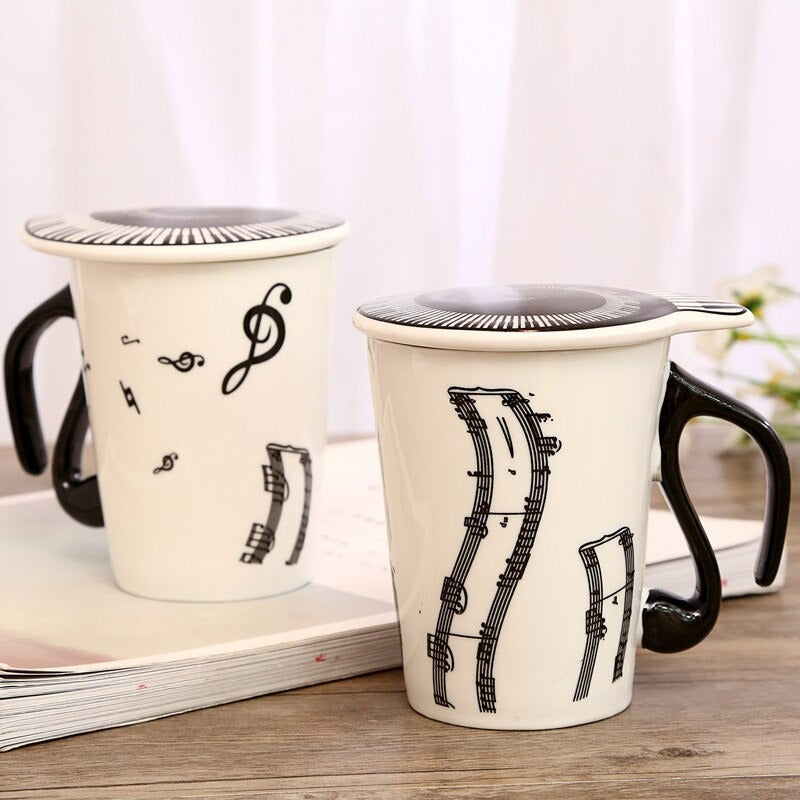 Two mugs and lids with music inspired imagery printed on them. They are black and white and the lids are on top of each mug.