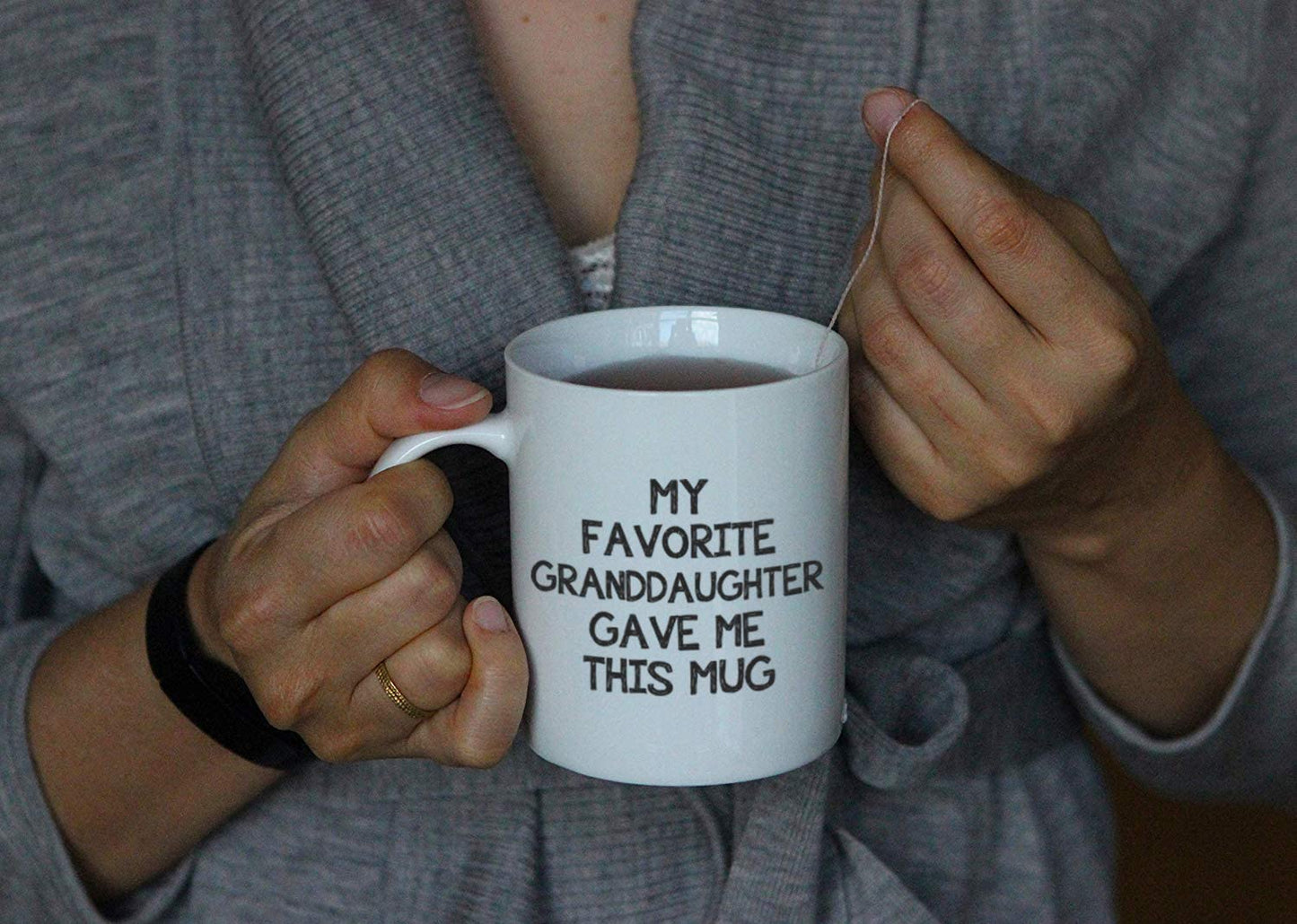 A pair of hands are holding a white ceramic coffee cup with the words, 'my favorite granddaughter gave me this mug' printed on it.