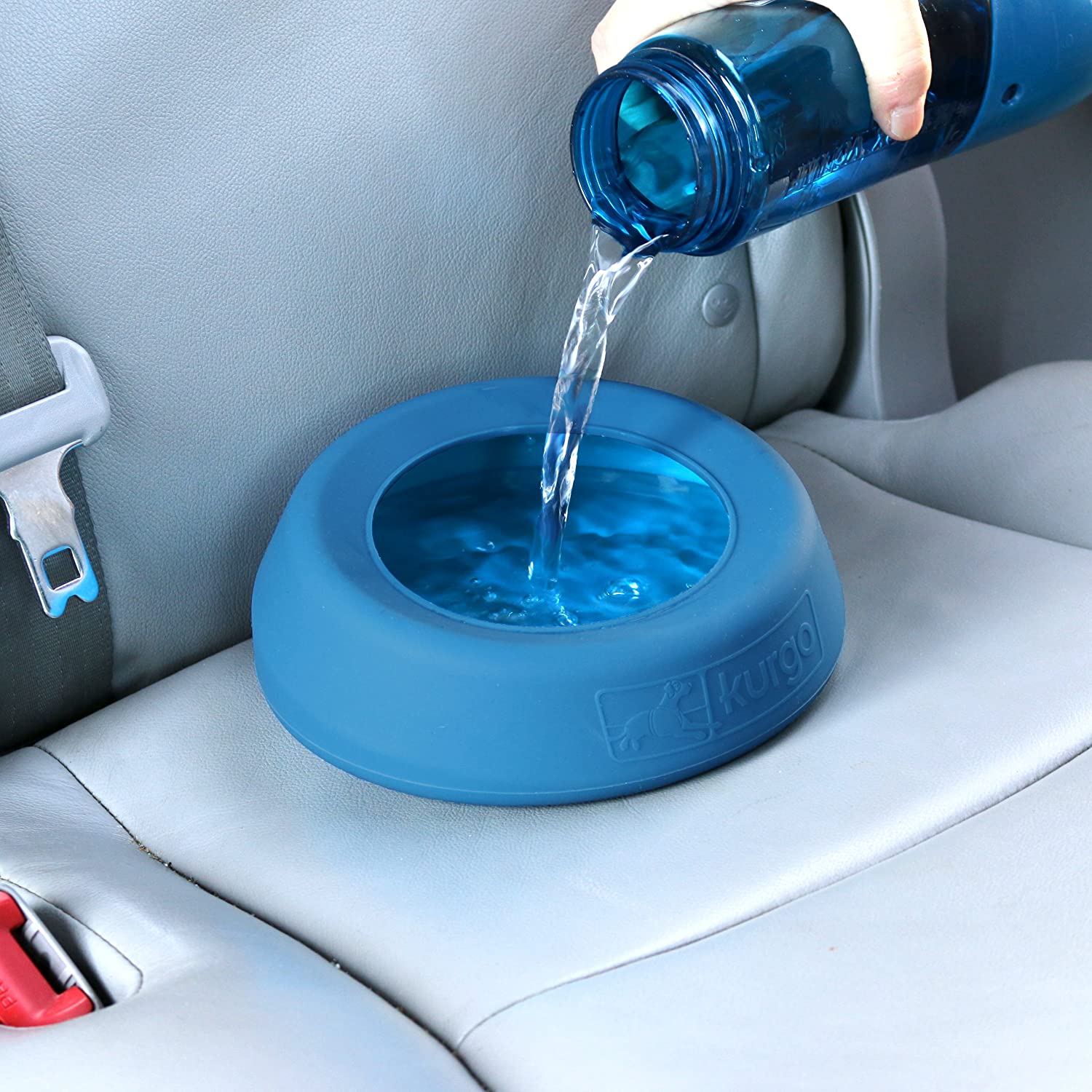 Water is being poured into a no-spill travel dog bowl which is on the backseat of a car.