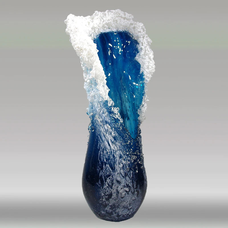 A vase which looks like an ocean wave. The vase is mostly ocean blue color with white edges to resemble sea foam.