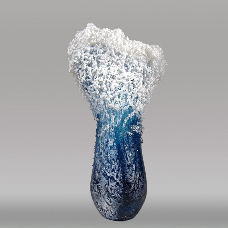 Rear view of an ocean wave vase which looks like a wave in motion. The main color is blue with foamy white tips and it’s made of resin.