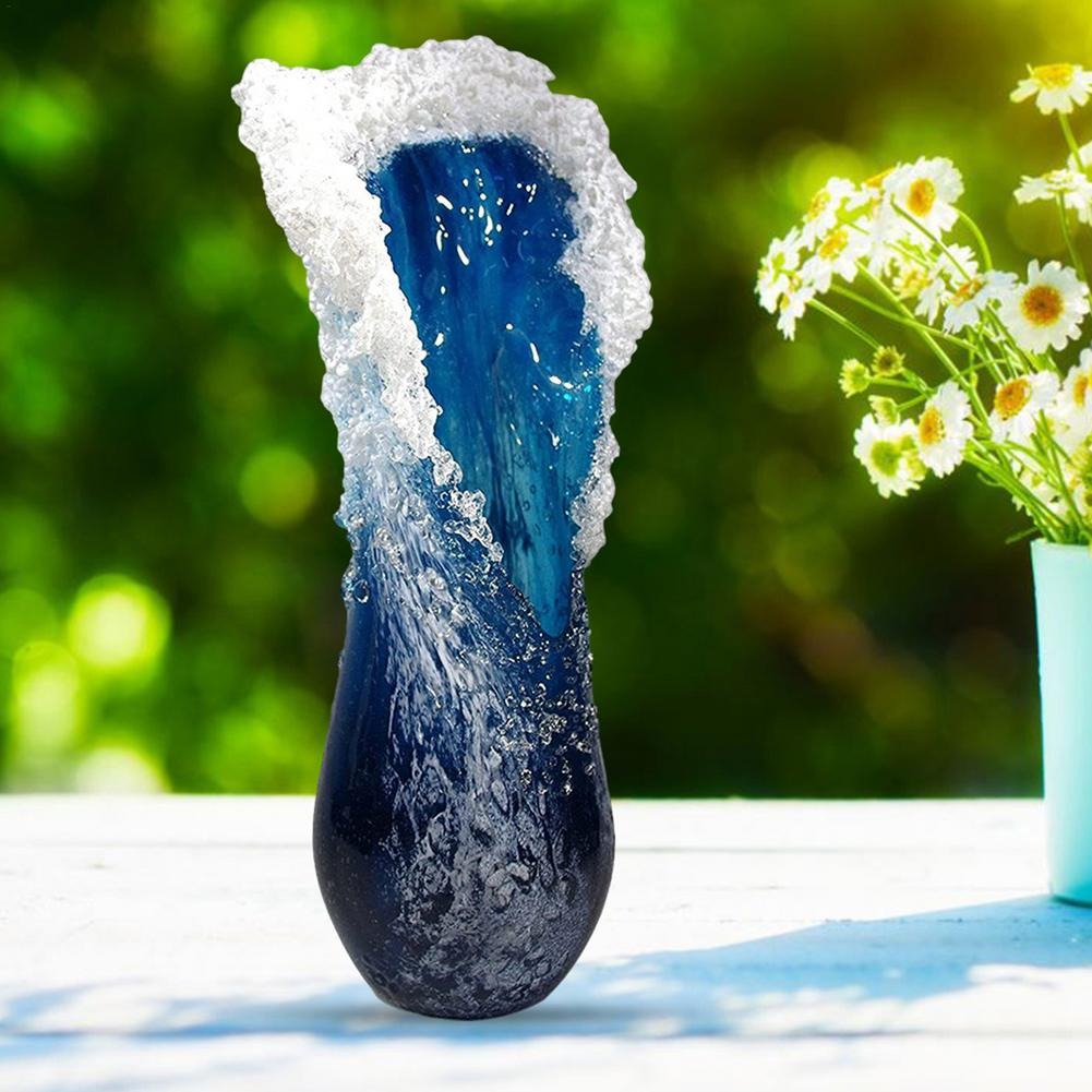 A resin ocean wave vase which looks like a frozen wave is outside on a table next to another vase filled with miniature daises.