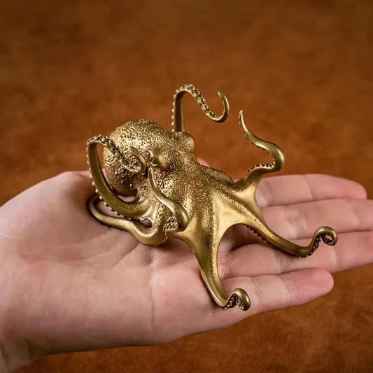 A gold colored octopus shaped phone holder being held in the palm of a persons hand.