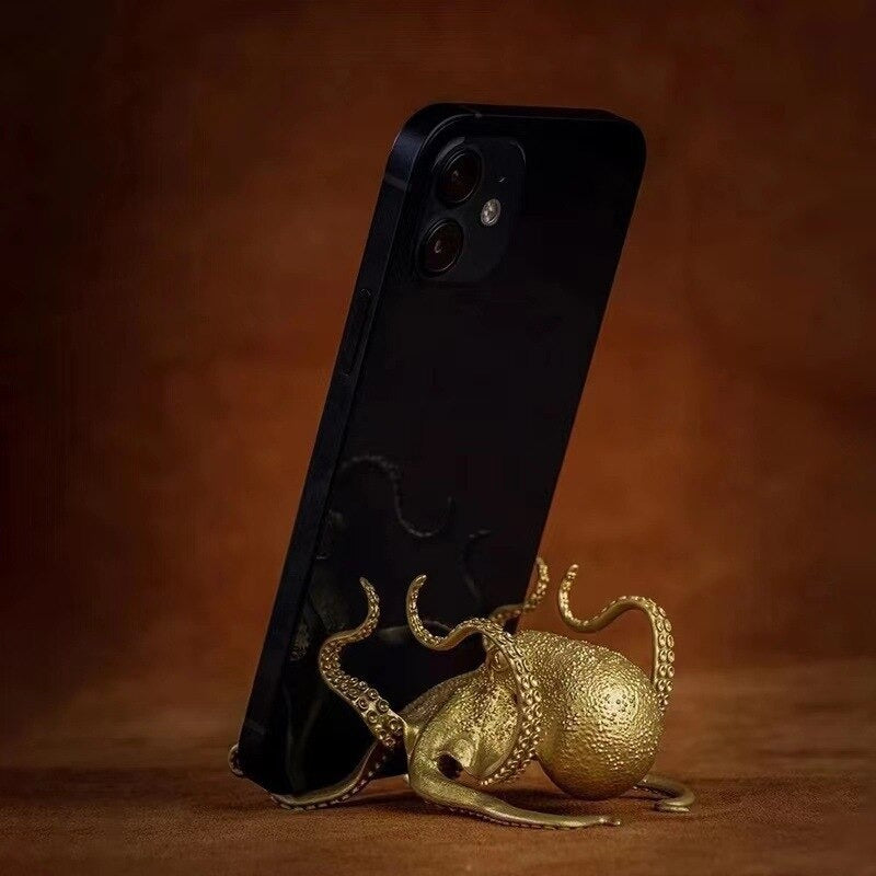 An octopus shaped cell phone holder which is holding up a black phone.