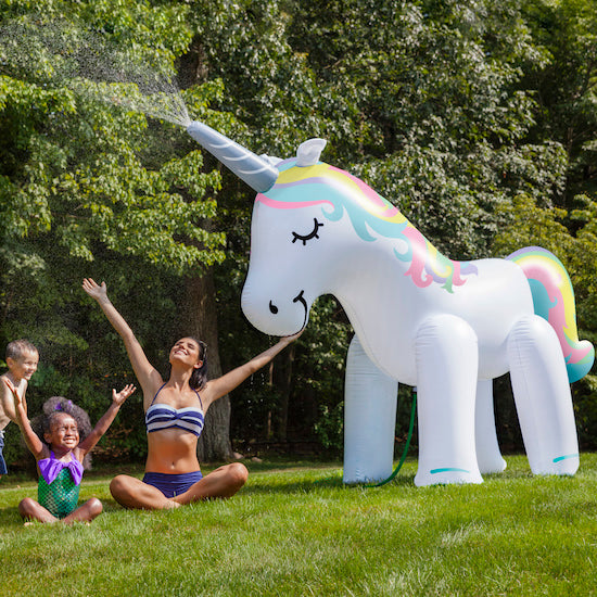 Large inflatable unicorn sprinkler spraying water over a backyard lawn