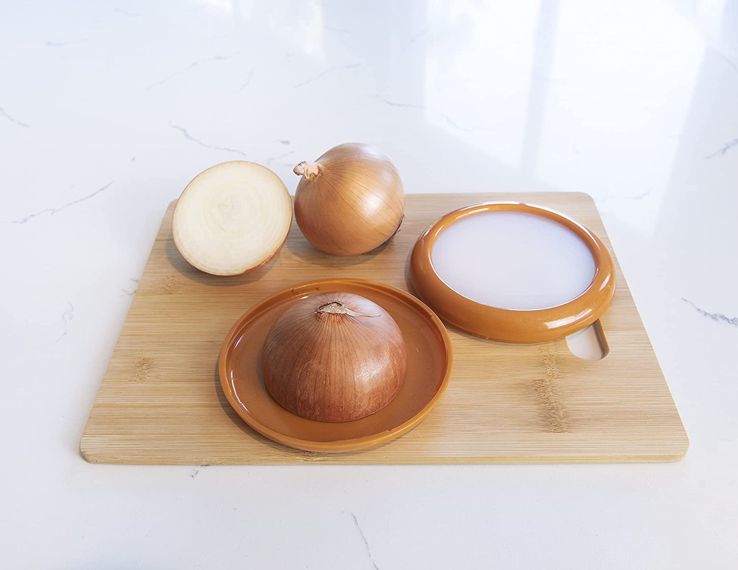 An onion saver pod is on a wooden chopping board along with a brown onion and another onion which has been sliced in half. One of the halves is on the base of the onion pod saver.