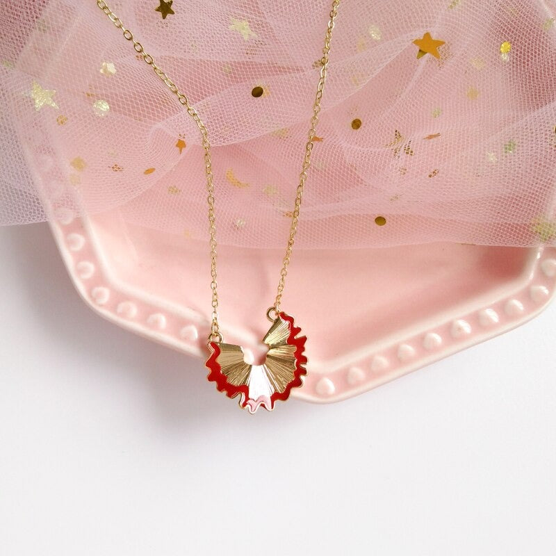 A gold chain and a gold pendant in the shape of a pencil shaving with the pendant having a red outline.