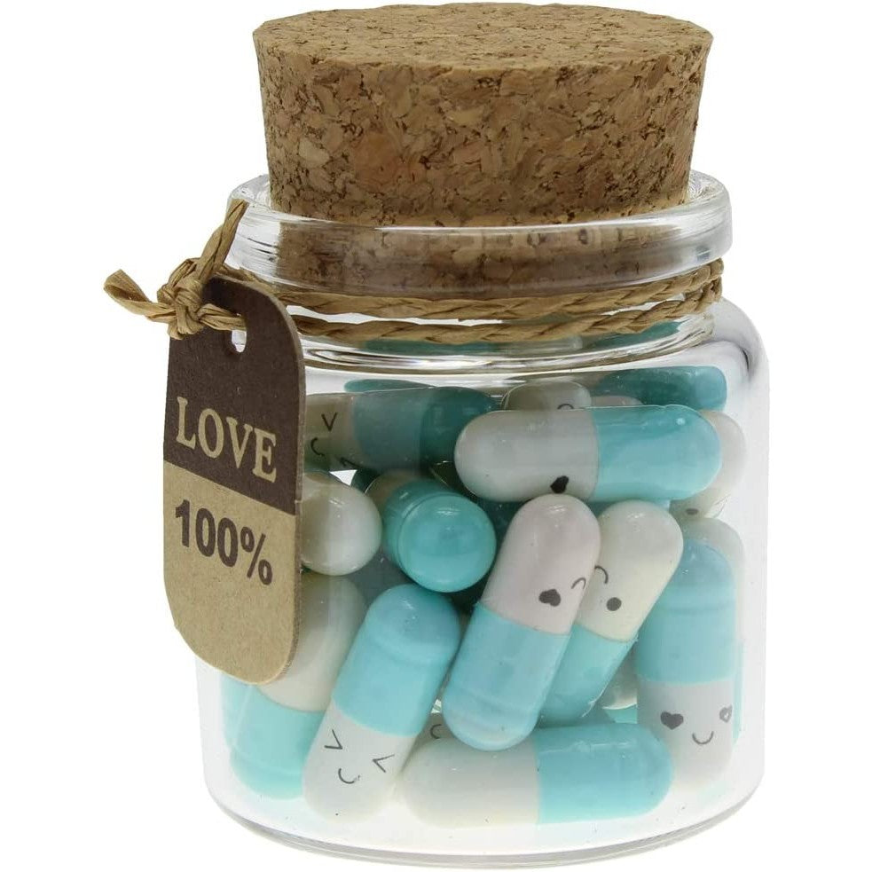 Small light blue and white pill capsules in a glass bottle with a cork. Each capsule contains a love note inside.