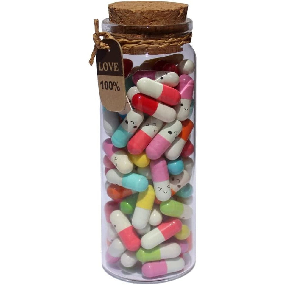 A tall glass jar filled up with various pill shaped capsules of different colors. Each pill has a cute little smiley face on it.