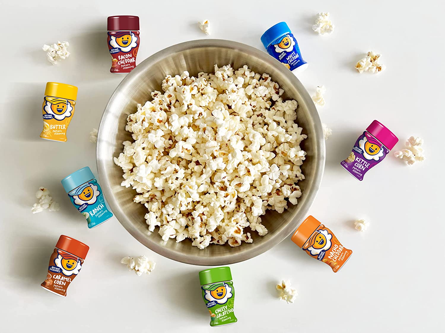 A very large bowl of popcorn with 8 different flavored popcorn seasoning jars scattered around the bowl.