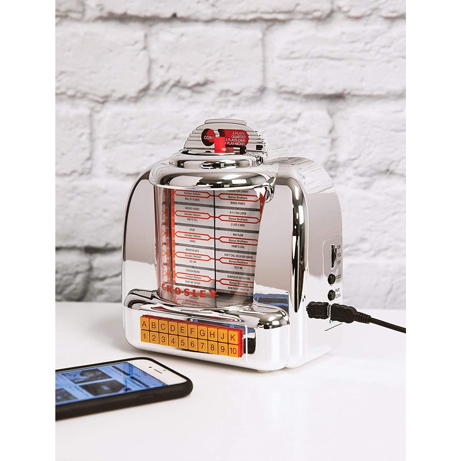 A retro jukebox radio is on a white table with a cellphone next to it.