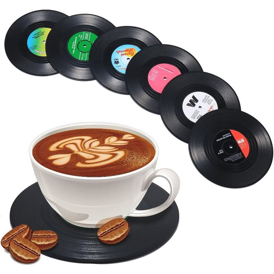 6 vinyl record drink coasters are fanned out. There is also a cup of coffee sitting on another vinyl record coaster.