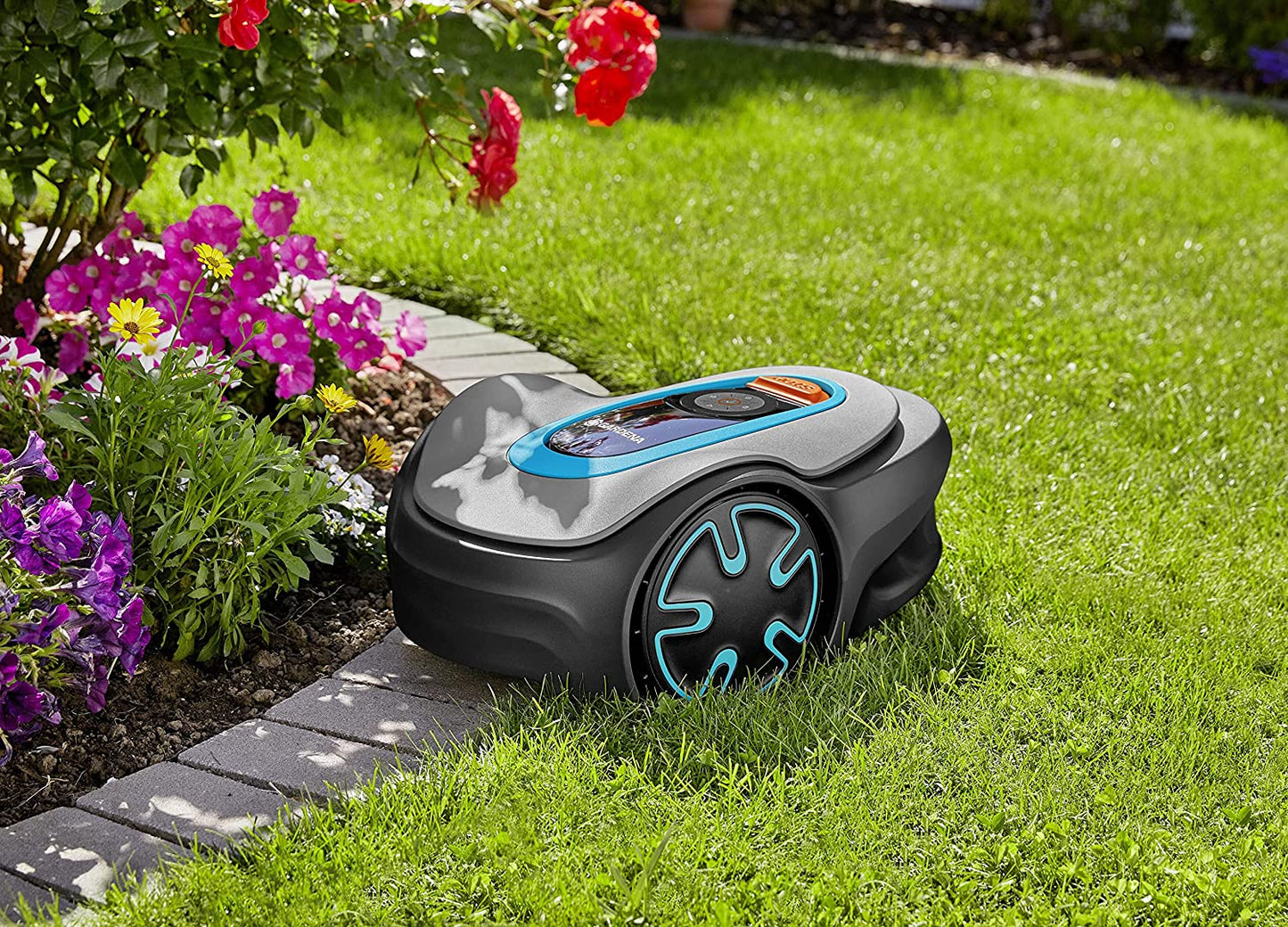 A robotic lawn mover under the shade of some flowers resting on a lawn.