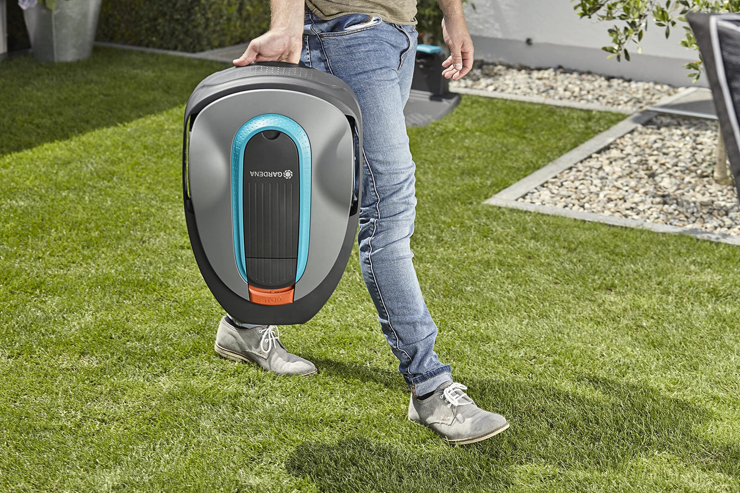 A person carrying a robotic lawn mower across the yard.