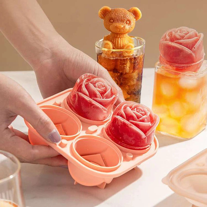 An apricot colored ice cube mold which makes rose shaped ice cubes. A pair of hands are holding the tray which has four compartments, two of which feature rose shaped ice cubes, the other two compartments are empty.