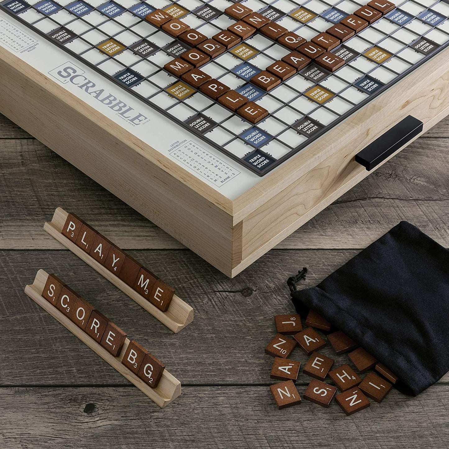 A close up view of a maple wood edition of Scrabble. Various letter tiles are on the board and on Scrabble letter holding trays.
