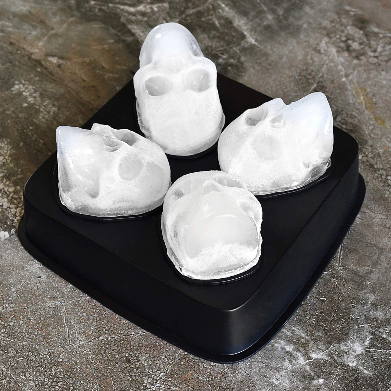 A black silicone ice cube mold with four skull shaped ice cube examples resting in the molds of the tray.