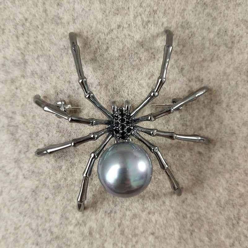 A black spider brooch with small faux black gems and a simulated black pearl. The brooch is shown closeup on the label of jacket.