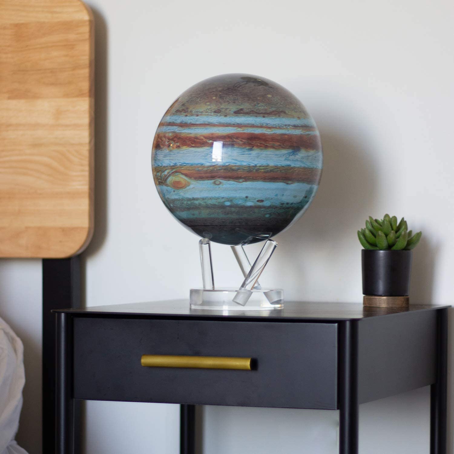 A rotating version of planet Jupiter including the Great Red Spot on a acrylic stand. The globe is on a black bedside table.