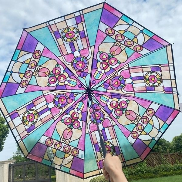 A hand holding a colorful umbrella which looks like it is made out of stained glass.
