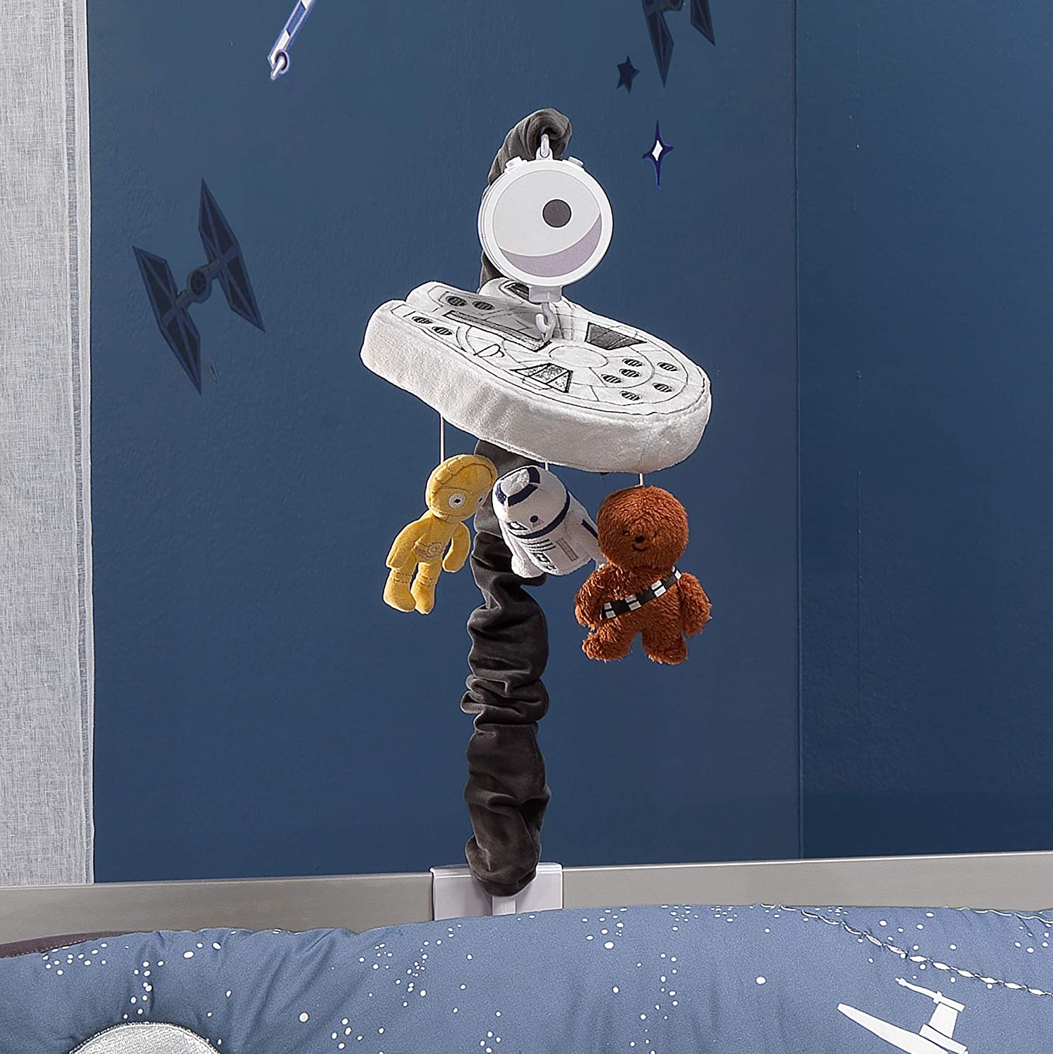 A baby crib with a mobile hanging above it. The mobile features a ship and characters from the Star Wars movies.