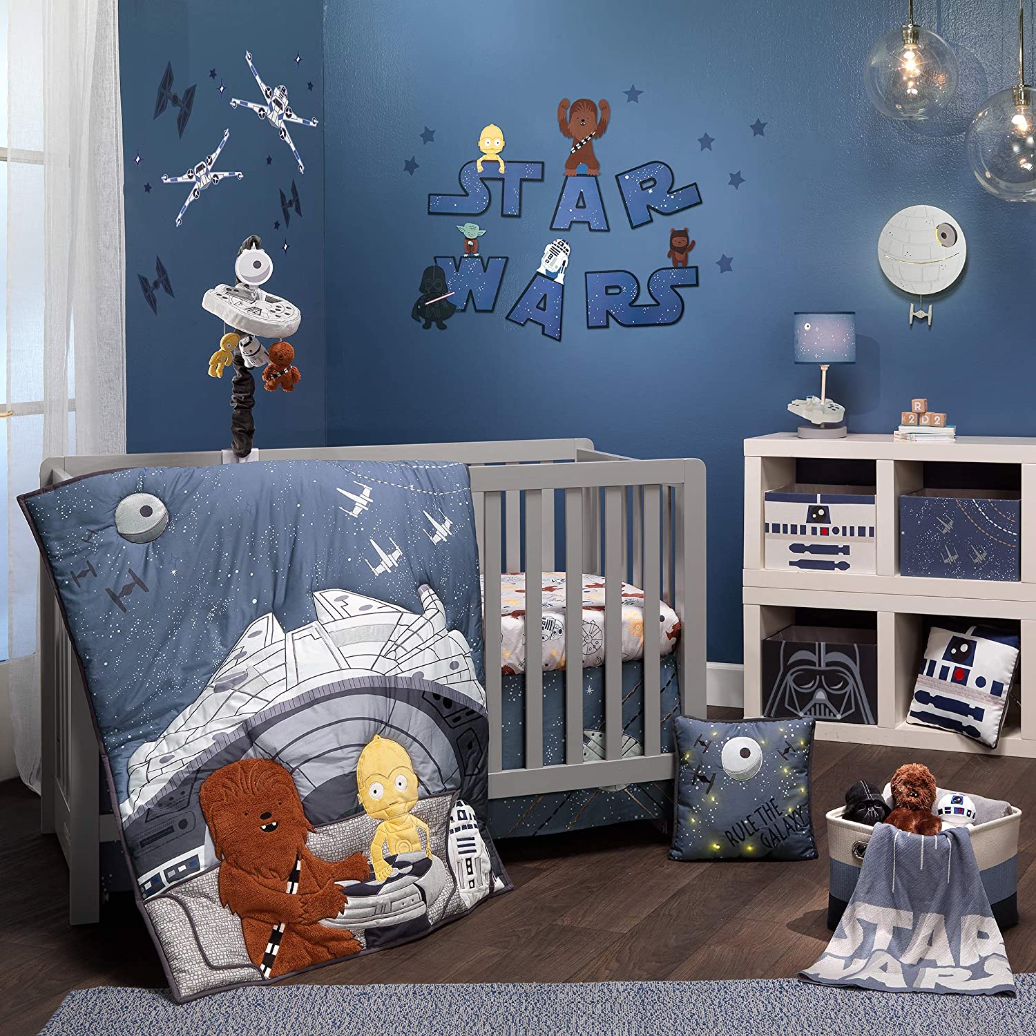 A baby child's Star Wars themed bedroom which has a Star Wars mobile hanging over the crib. On the wall are the words, "Star Wars" and there is other Star Wars themed items scattered about the room.