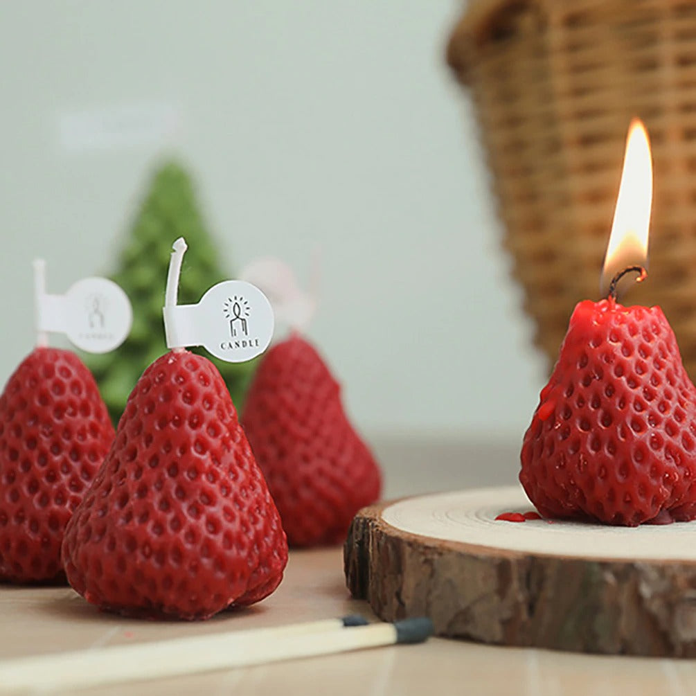 Four red strawberry shaped candles, one is alight with a flame.
